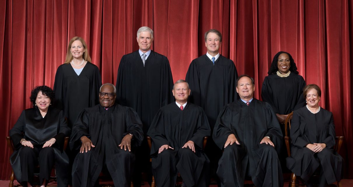 Formal group photograph of the Supreme Court as it was been comprised on June 30, 2022 after Justice Ketanji Brown Jackson joined the Court. The Justices are posed in front of red velvet drapes and arranged by seniority, with five seated and four standing. Seated from left are Justices Sonia Sotomayor, Clarence Thomas, Chief Justice John G. Roberts, Jr., and Justices Samuel A. Alito and Elena Kagan. Standing from left are Justices Amy Coney Barrett, Neil M. Gorsuch, Brett M. Kavanaugh, and Ketanji Brown Jackson.