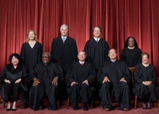 Formal group photograph of the Supreme Court as it was been comprised on June 30, 2022 after Justice Ketanji Brown Jackson joined the Court. The Justices are posed in front of red velvet drapes and arranged by seniority, with five seated and four standing. Seated from left are Justices Sonia Sotomayor, Clarence Thomas, Chief Justice John G. Roberts, Jr., and Justices Samuel A. Alito and Elena Kagan. Standing from left are Justices Amy Coney Barrett, Neil M. Gorsuch, Brett M. Kavanaugh, and Ketanji Brown Jackson.